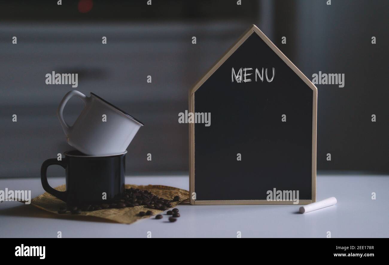 Menütext auf leerer schwarzer Tafel neben zwei Tassen und Kaffeebohnen. Platz für Text- oder Bildmaterial kopieren Stockfoto