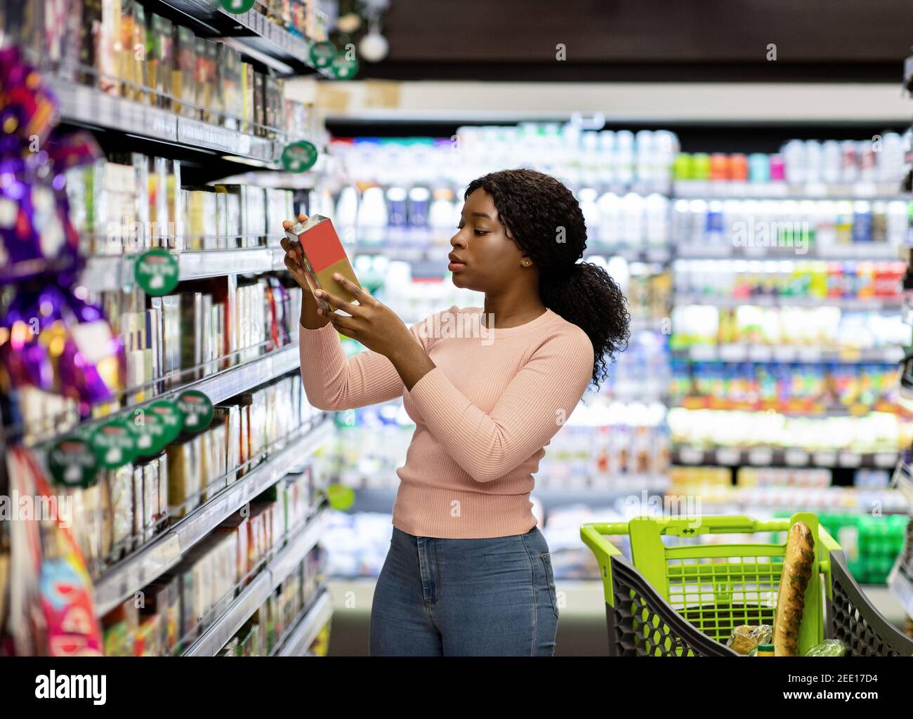 Hübsche afroamerikanische Frau, die Lebensmittel im Supermarkt wählt, Lebensmittel kauft, Produkte für ihre Familie kauft Stockfoto