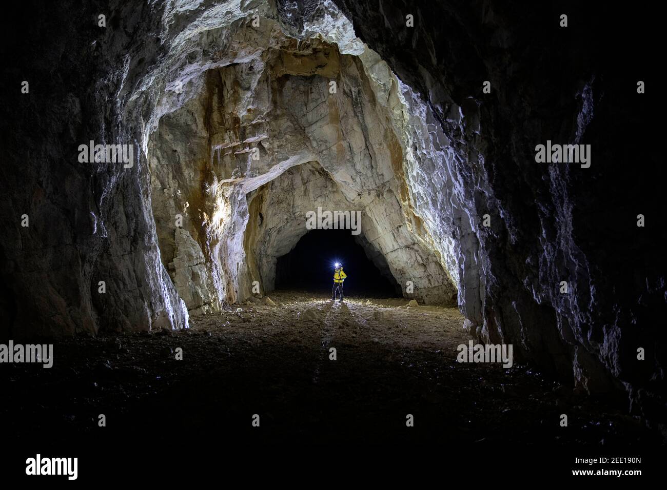 Frau, die in einer Höhle mit einem Scheinwerfer steht, beleuchtet von einer Hintergrundbeleuchtung, Slowenien Stockfoto