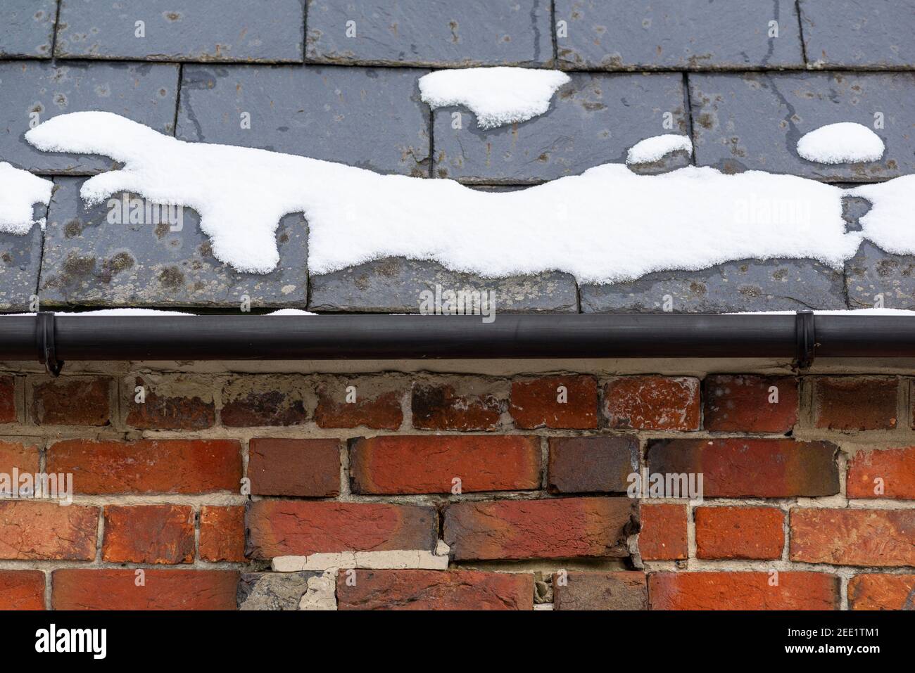 Schnee auf Schieferdach mit gemauerter Mauer unter schwarzer Rinne. Stockfoto