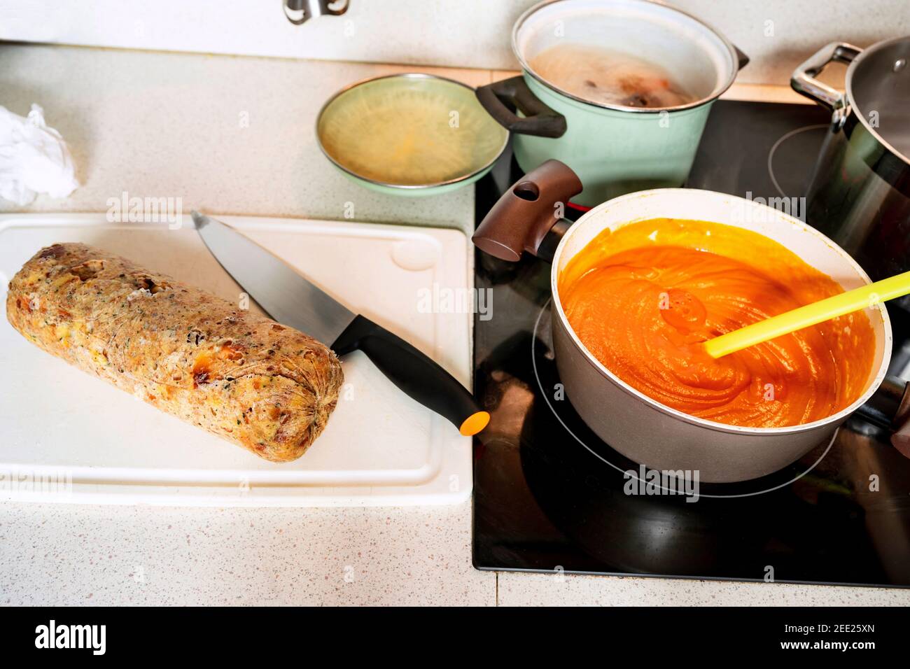 Frisch gekochte ganze Knödel mit Messer auf Küchenbrett, heiße sprudelnde Tomatensauce mit Löffel in der Pfanne, Töpfe mit gekochtem Rindfleisch auf Keramik-Kochfeld. Vorbereitung Stockfoto