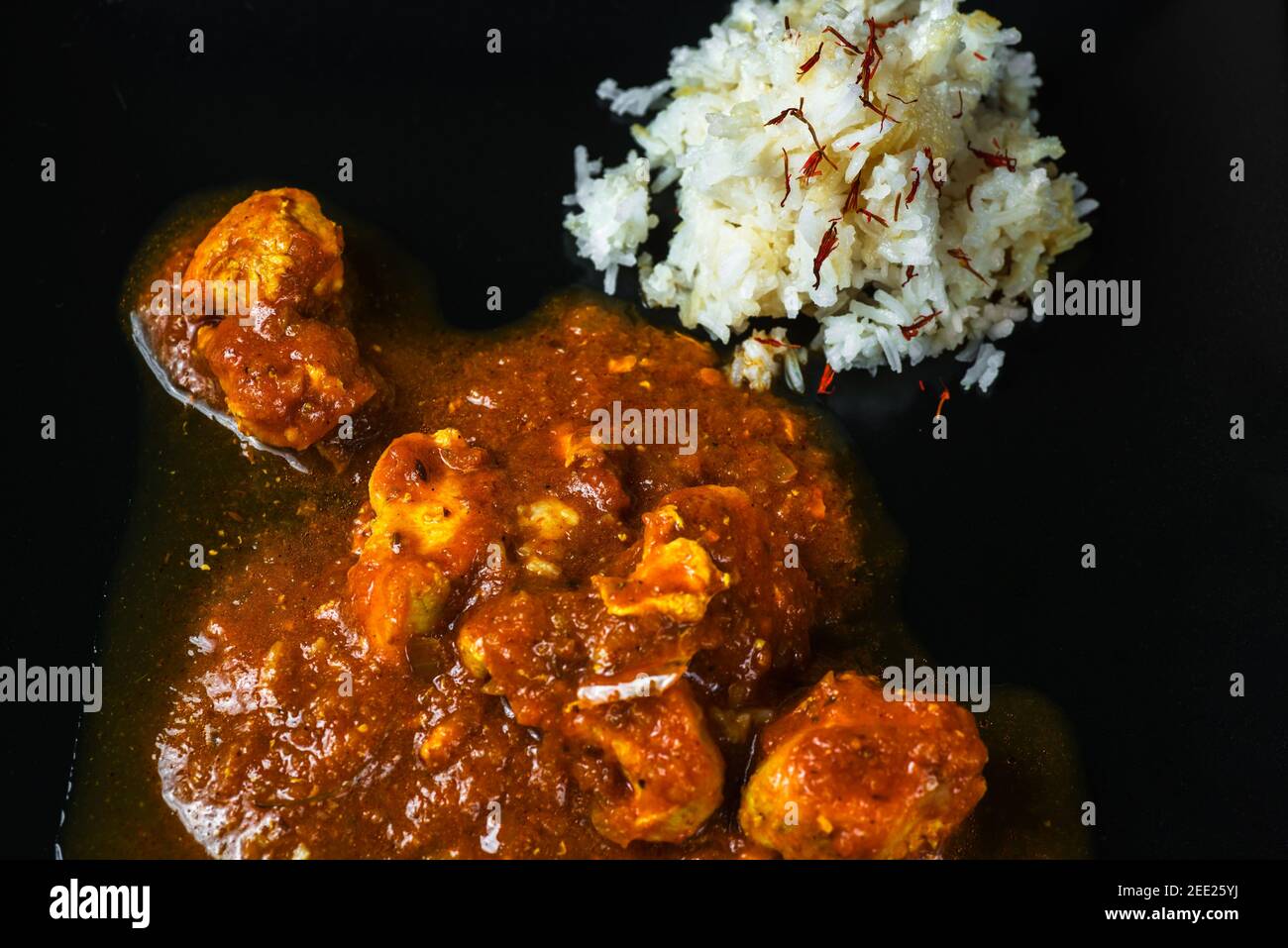Hühnerfleisch (in madras-Art), Hühnerfleisch in würziger Sauce, Reis mit Safran auf schwarzem Hintergrund, Nahaufnahme. Indische Mahlzeit. Details. Stockfoto