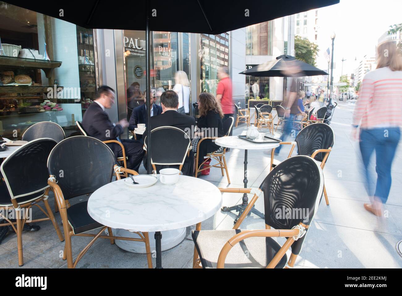 Ein französisches Café mit Tischen auf dem Bürgersteig ist während der morgendlichen Hauptverkehrszeit in Washington, DC, voll. Bewegungsunschärfe. Stockfoto