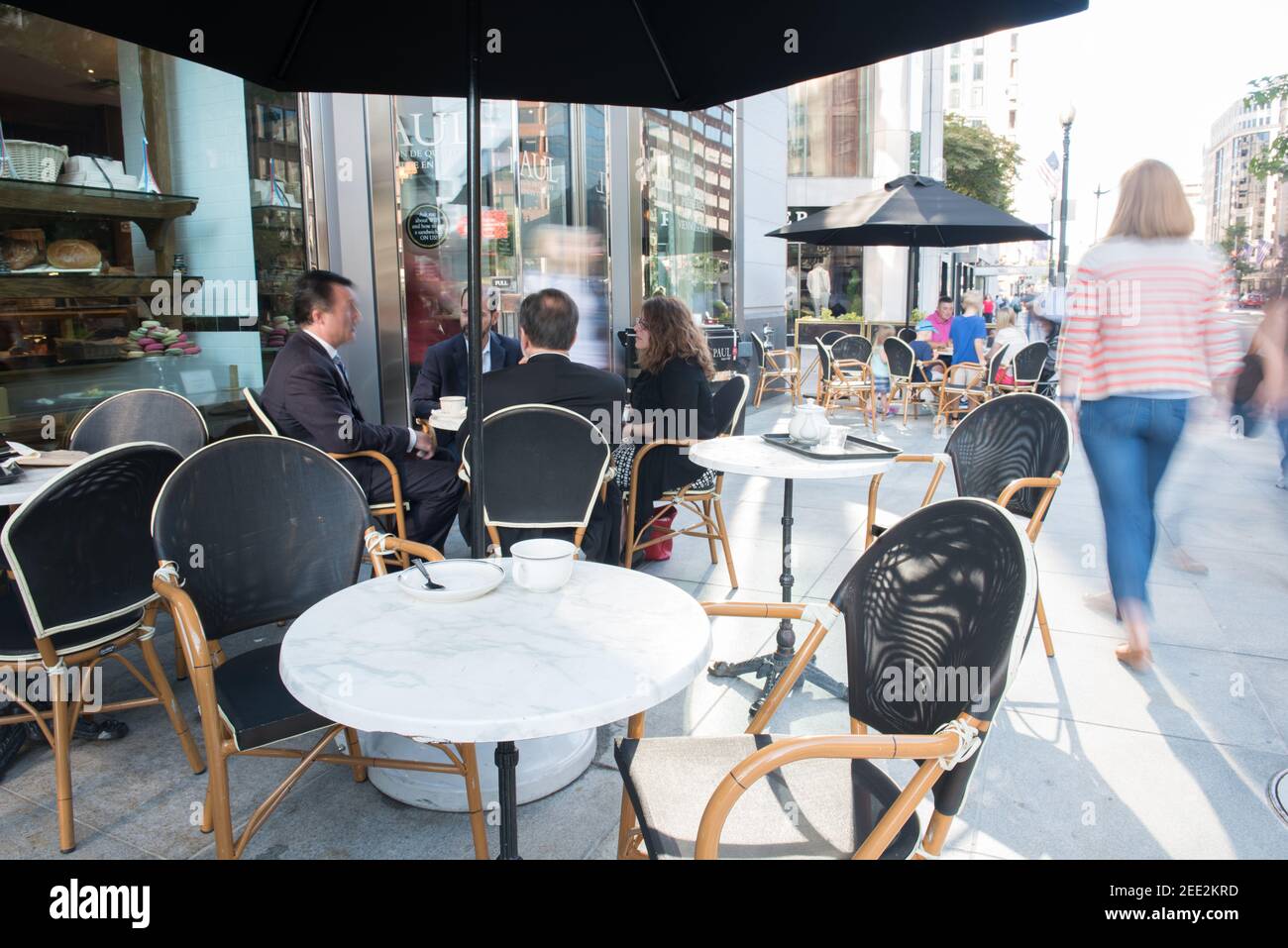 Ein französisches Café mit Tischen auf dem Bürgersteig ist während der morgendlichen Hauptverkehrszeit in Washington, DC, voll. Bewegungsunschärfe. Stockfoto