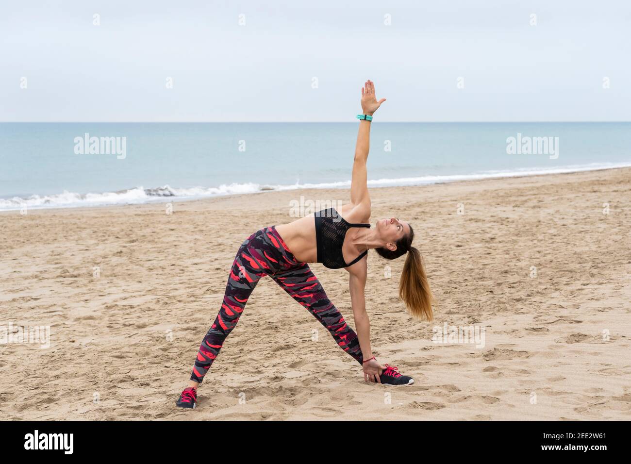 Junge Fitness-Frau praktiziert Yoga verlängerte Dreieck Pose am Strand am Meer. Utthita trikonasana Asana, Ashtanga Vinyasa Yoga Sport Lifestyle.Heilung Stockfoto