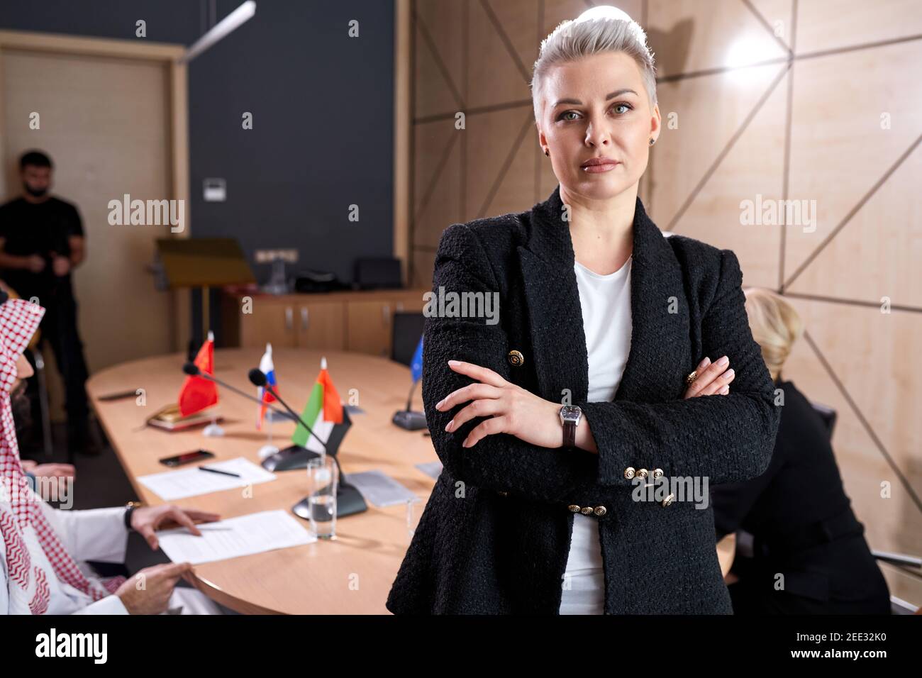 50-55 Jahre alte Geschäftsfrau mit stylischen kurzen Haaren Formelle Kleidung in Sitzungssaal während des Treffens mit internationalen Gruppe posiert Der Politiker sitzen Stockfoto