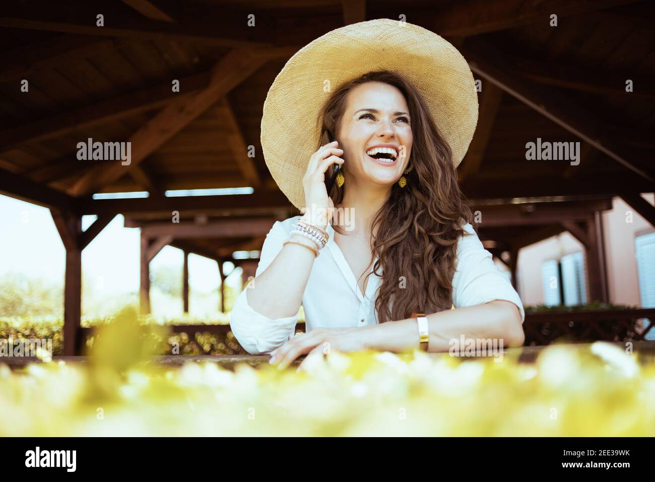 Happy stilvolle Frau in weißem Hemd mit Hut reden auf einem Smartphone auf dem Bauernhof. Stockfoto