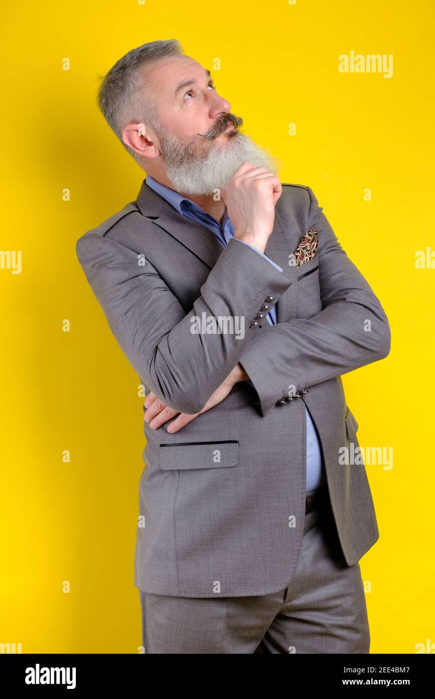 Studio Portrait reifen bärtigen Mann in grauem Anzug gekleidet sieht pensiv beiseite, denkt über etwas, gelben Hintergrund Stockfoto