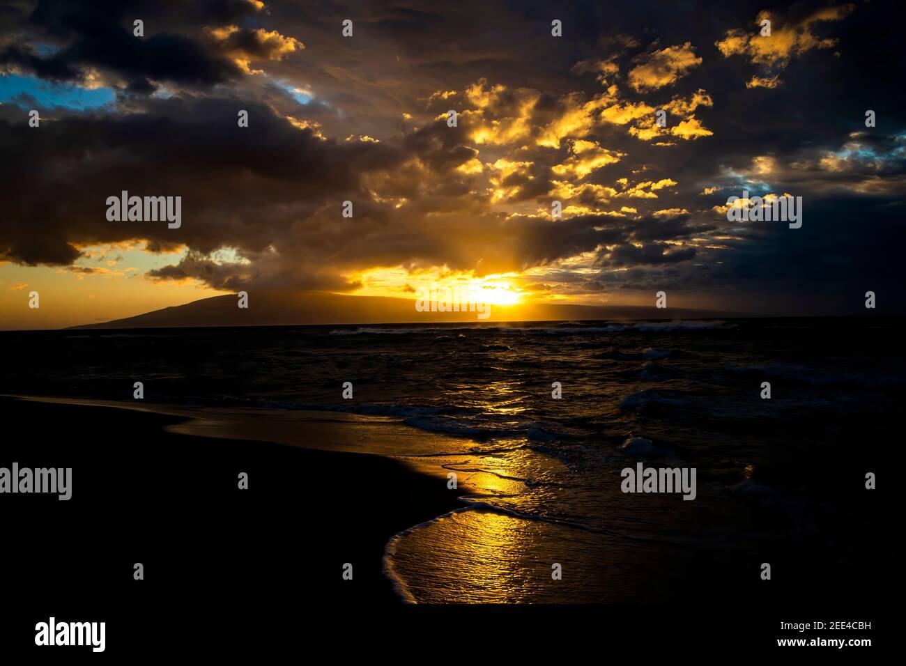 Goldene Sonnenuntergangslandschaft mit Lichtstrahlen, die von unter den Wolken strahlen, während die Sonne hinter der tropischen Insel untergeht. Stockfoto