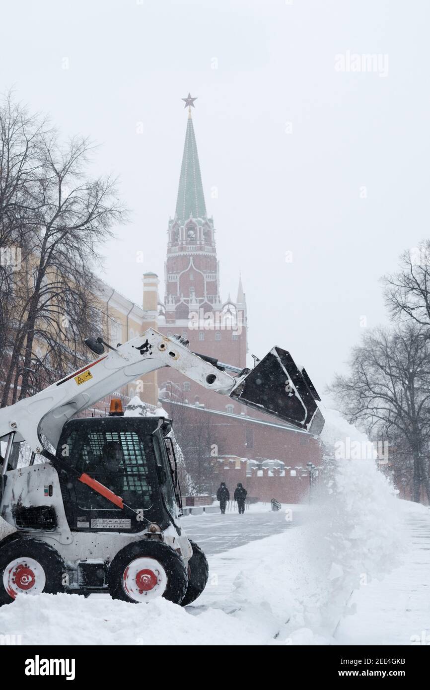 Moskau. Russland. Februar 12, 2021. Ein kleiner Bagger Bagger Bobcat entfernt Schnee vom Bürgersteig in der Nähe der Kremlmauern bei einem starken Schneefall Stockfoto