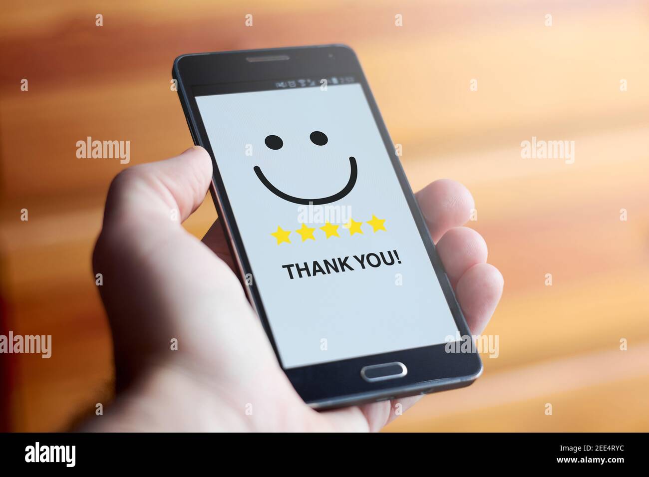 Nahaufnahme der männlichen Hand hält Handy mit lächelndem glücklichen Gesicht und fünf Sterne Bewertung mit dem Text "Danke!" Auf weißem Bildschirm gegen außerhalb des Fokus Stockfoto