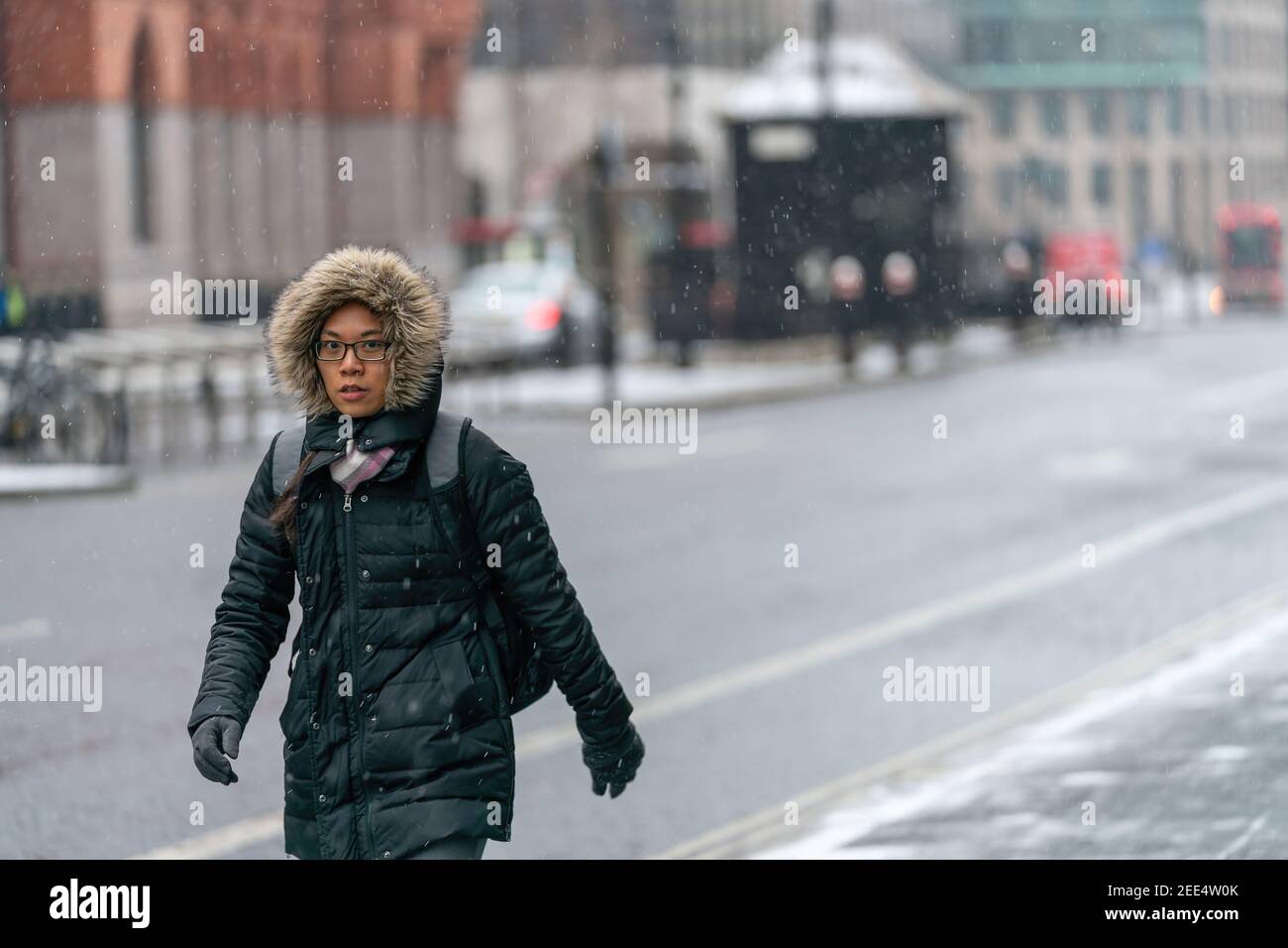 LONDON, ENGLAND - 8. FEBRUAR 2021: Schöne junge orientalische Frau in einer mit Pelz getrimmten Kapuze mit Brille beim Schneeschauer in Holborn London auf Stockfoto
