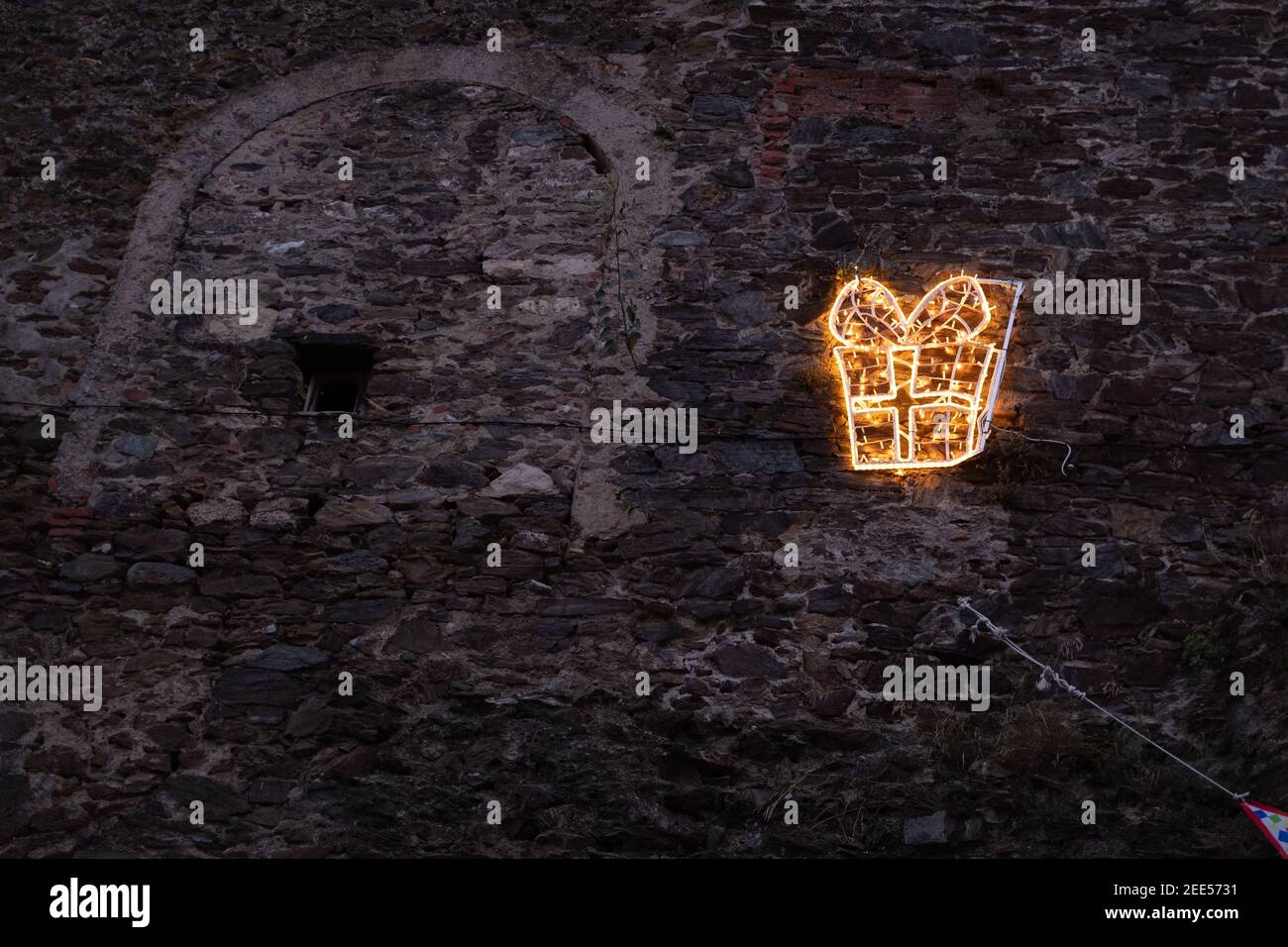 Ein Leuchtenornament, das ein Weihnachtsgeschenk auf einem Dunkle Steinmauer Stockfoto