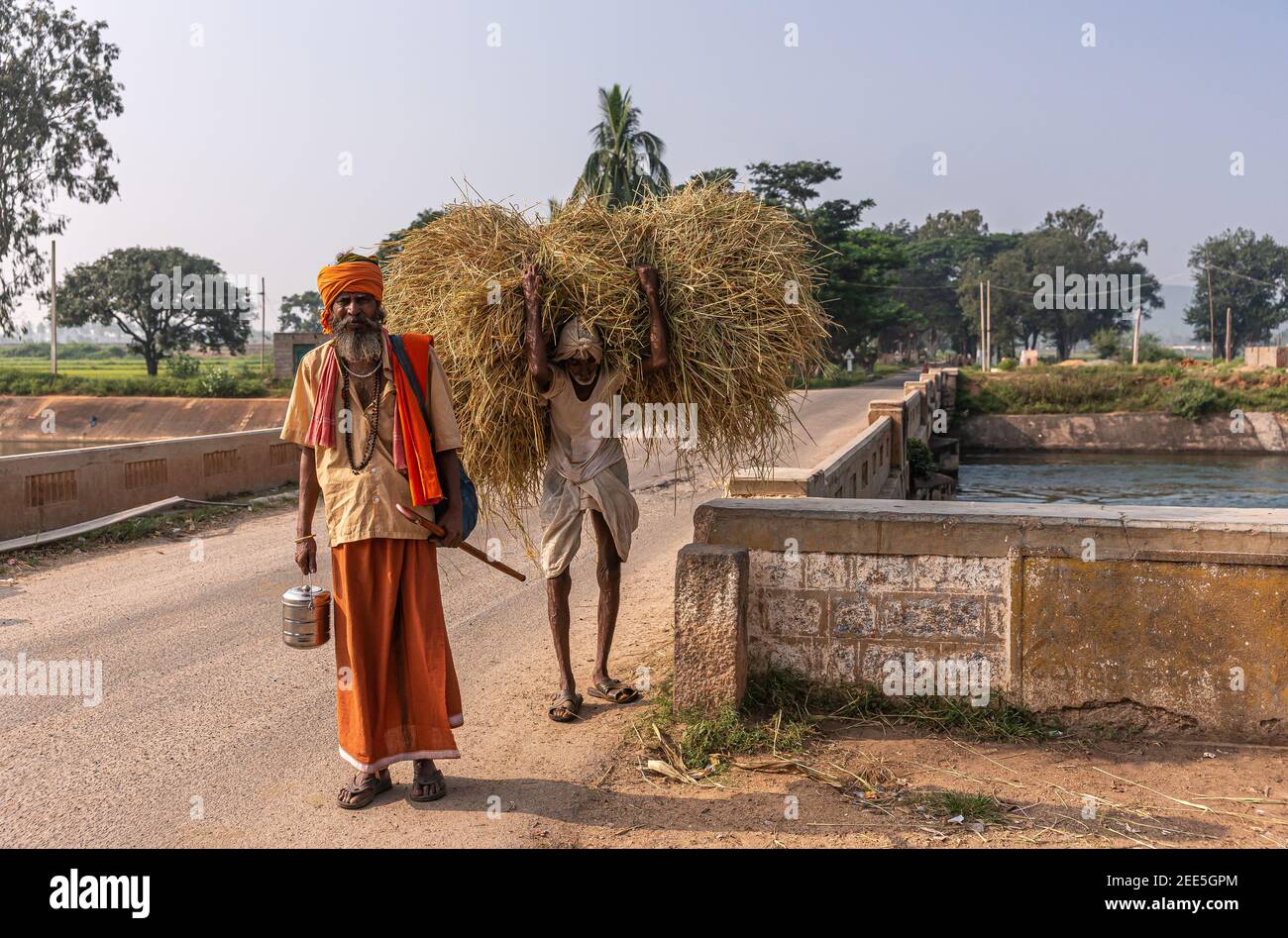 Bullapur, Karnataka, Indien - 9. November 2013: Wandernder Sadhu mit safranfarbenem Rock, Turban und Handtuch auf gelbem Hemd und Mann mit Haufen von s Stockfoto