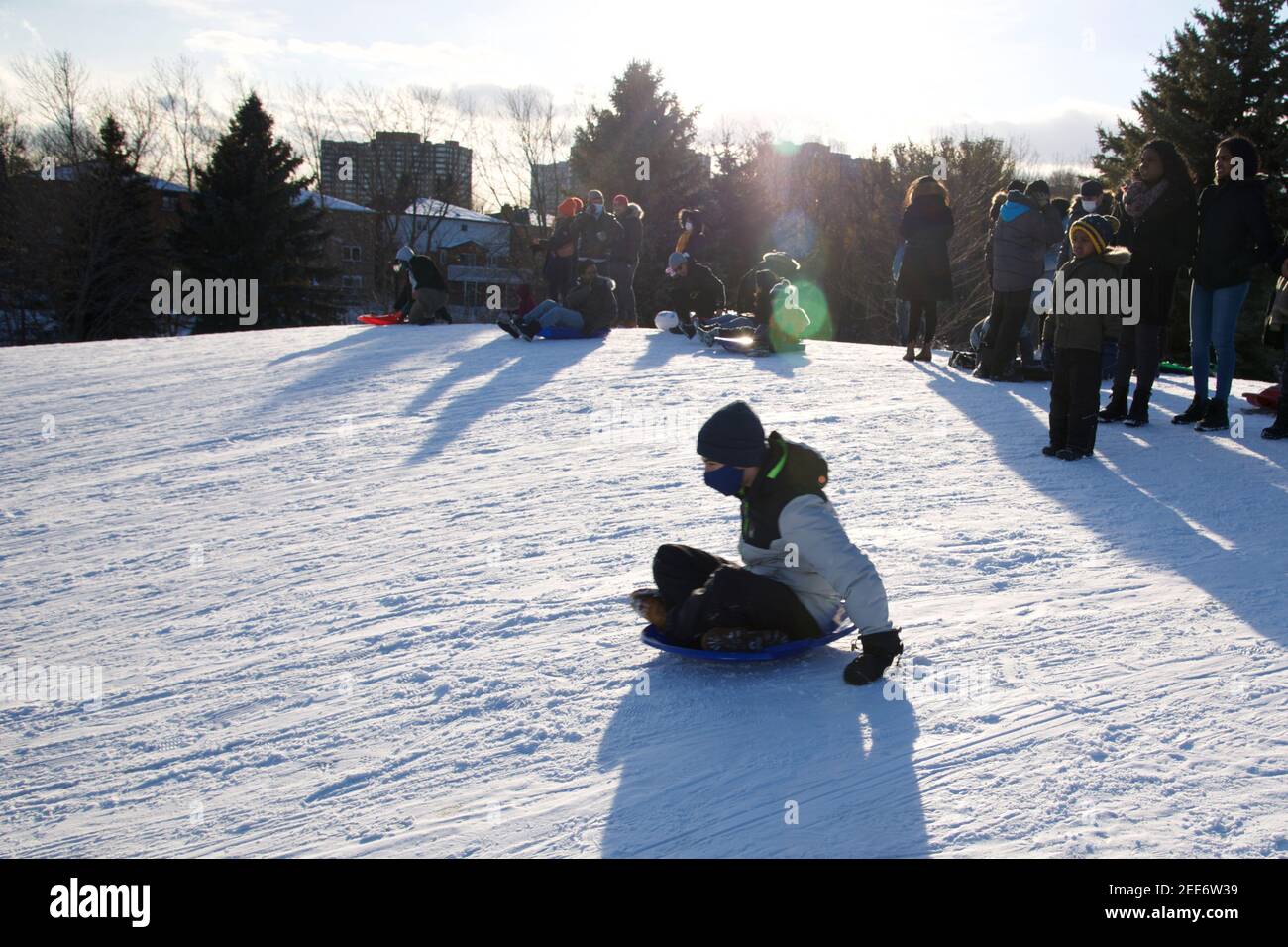 Toronto, Ontario / Canada - 02-14-2021: Wintersport-Rodel - Kinder spielen Rodel mit Gesichtsmaske. Covid-19, Winter, draußen, gesunde Lebensweise. Stockfoto