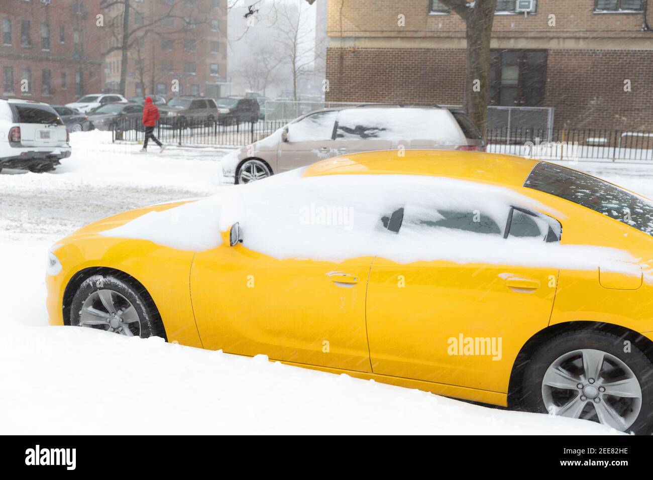 Gelbes Auto mit Schnee bedeckt mit Gebäuden im Hintergrund auf der City Street. Gefühle von einem Schneetag und Verkehr. Ideen für die Arbeit von zu Hause aus. Stockfoto