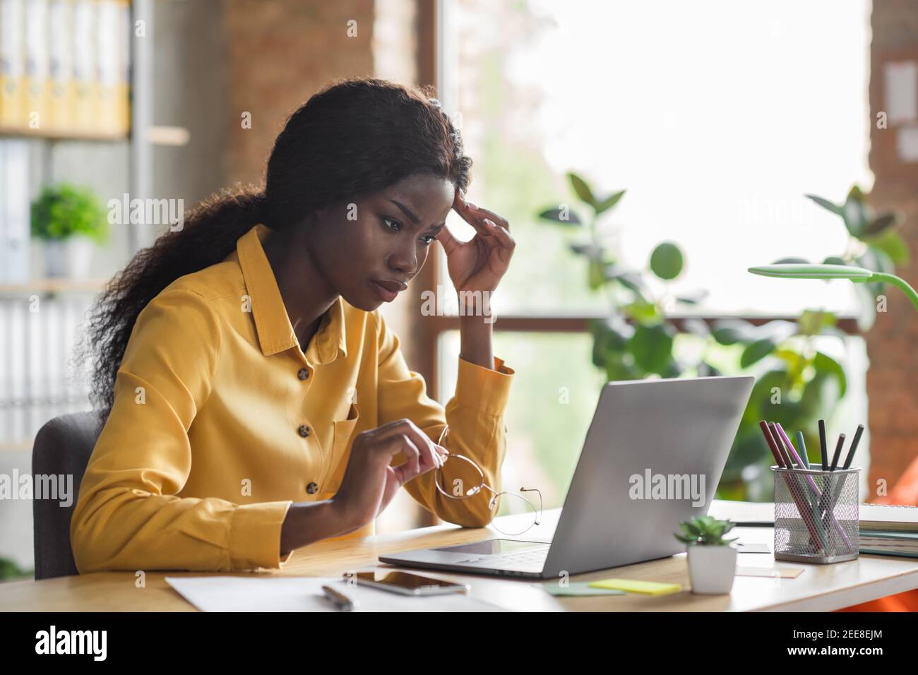 Foto-Porträt von afroamerikanischen Frau berühren Kopf an der Arbeit Laptop im modernen Büro im Innenbereich Stockfoto