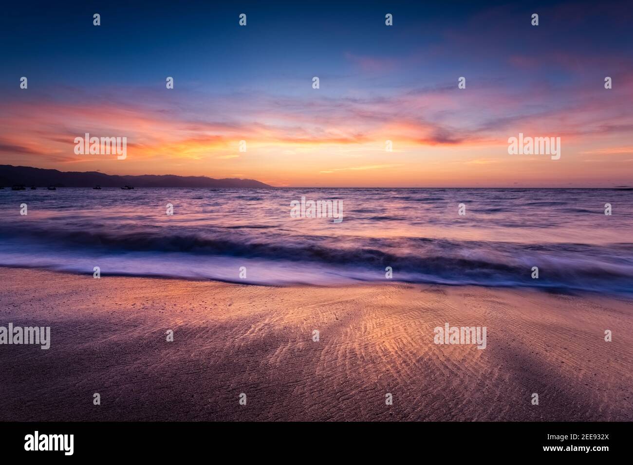 Ein farbenfroher Sonnenuntergang am Meer mit einer Welle, die an der Küste bricht Die Sonne untergeht am Horizont Stockfoto