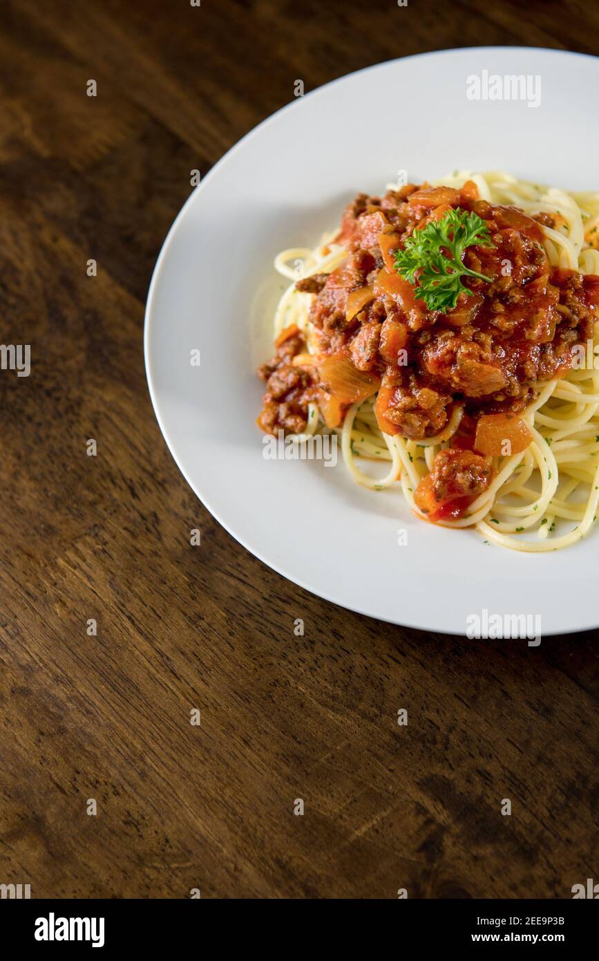 Hausgemachte leckere italienische Spaghetti mit Bolognese Fleischsoße und Petersilie Oben in weißem Teller auf Holztisch Stockfoto