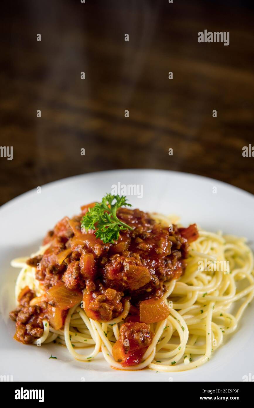 Hausgemachte leckere italienische Spaghetti mit heißen Bolognese Fleischsoße und Petersilie oben auf weißem Teller am Tisch Stockfoto