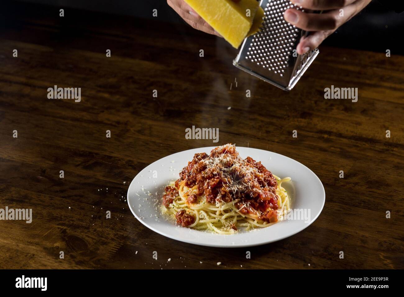 Der Koch reibe Parmesankäse auf Spaghetti Bolognese Weißes Gericht am Tisch Stockfoto