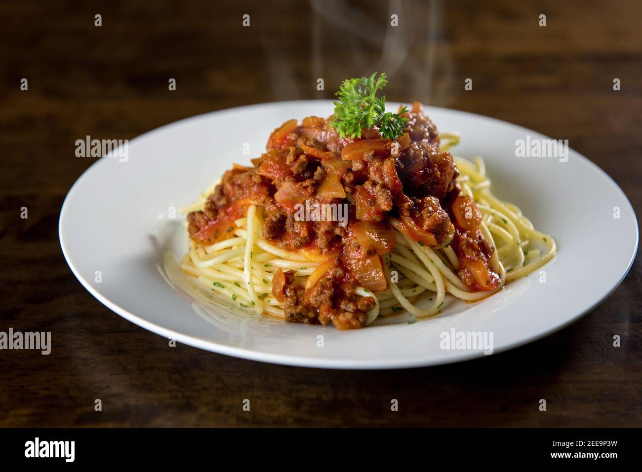 Hausgemachte leckere italienische Spaghetti mit heißen Bolognese Fleischsoße und Petersilie oben auf weißem Teller am Tisch Stockfoto