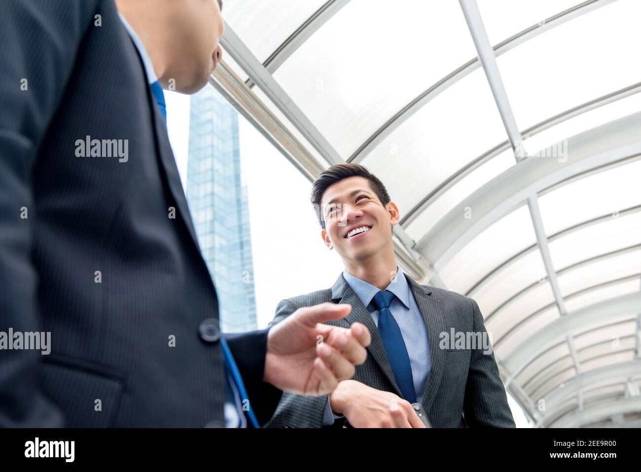Junge gut aussehende asiatische chinesische Geschäftsmann im Gespräch mit Partner im Freien an Überdachter Gang Stockfoto