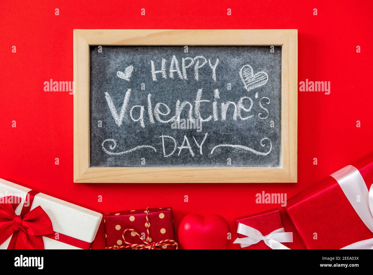 Alles Liebe zum Valentinstag handgeschriebener Text in Tafel mit Geschenkschachteln Auf rotem Hintergrund Stockfoto
