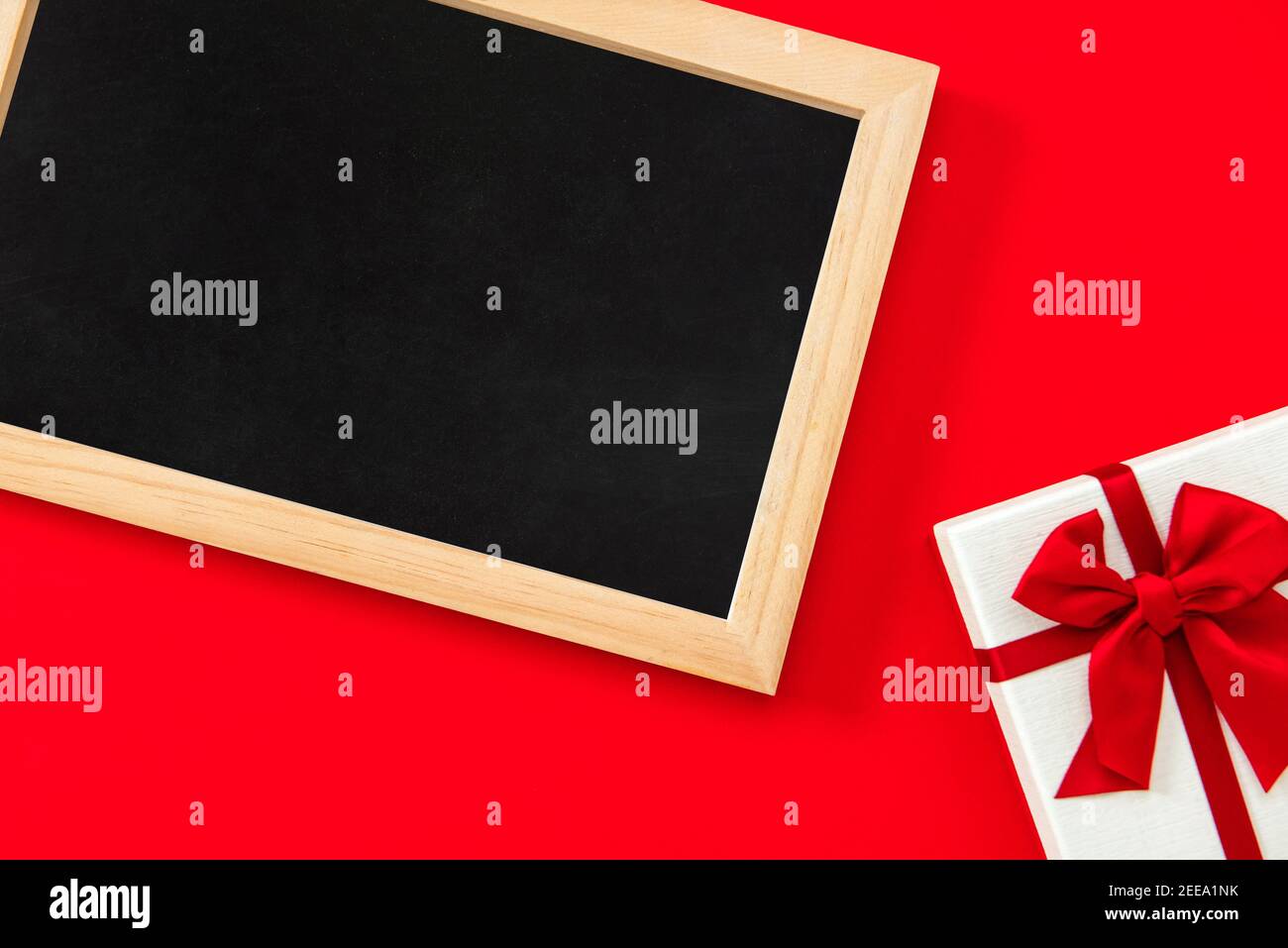 Leere Tafel auf rotem Hintergrund mit Geschenkbox am Rand Als Preis für Liebe und Romantik Stockfoto