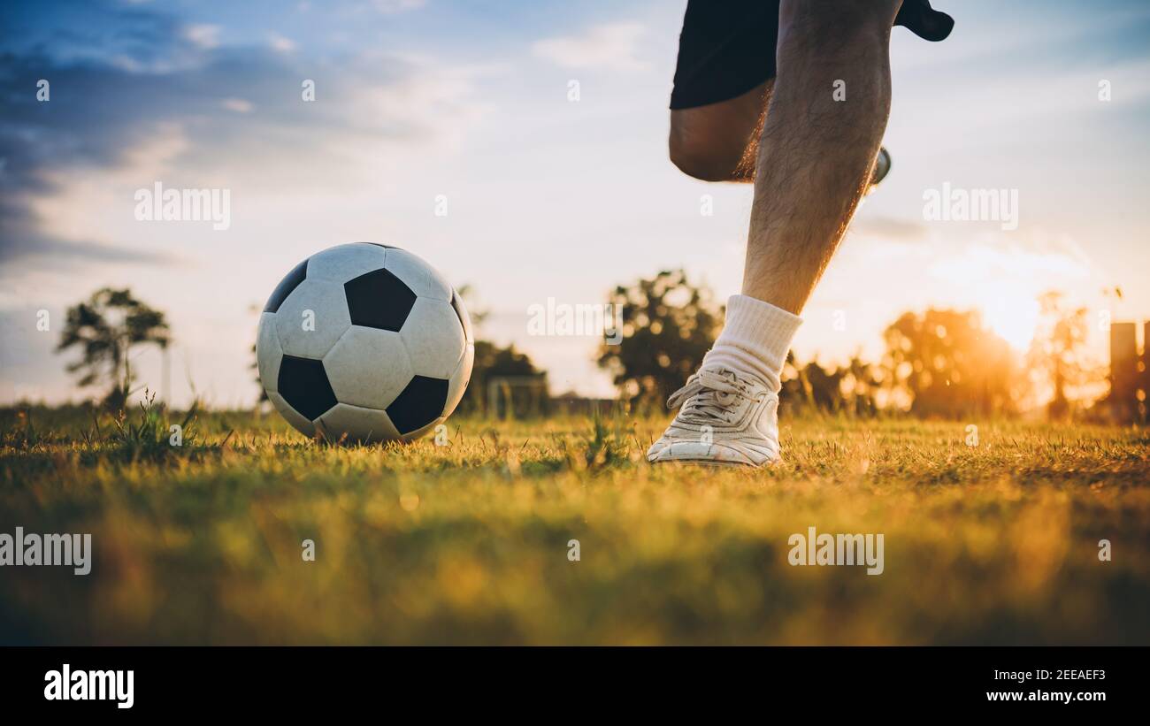 Action-Sport im Freien einer Gruppe von Kindern, die Spaß beim Fußball spielen Fußball für die Ausübung in der Gemeinde ländlichen Raum unter der Dämmerung Sonnenuntergang. Stockfoto