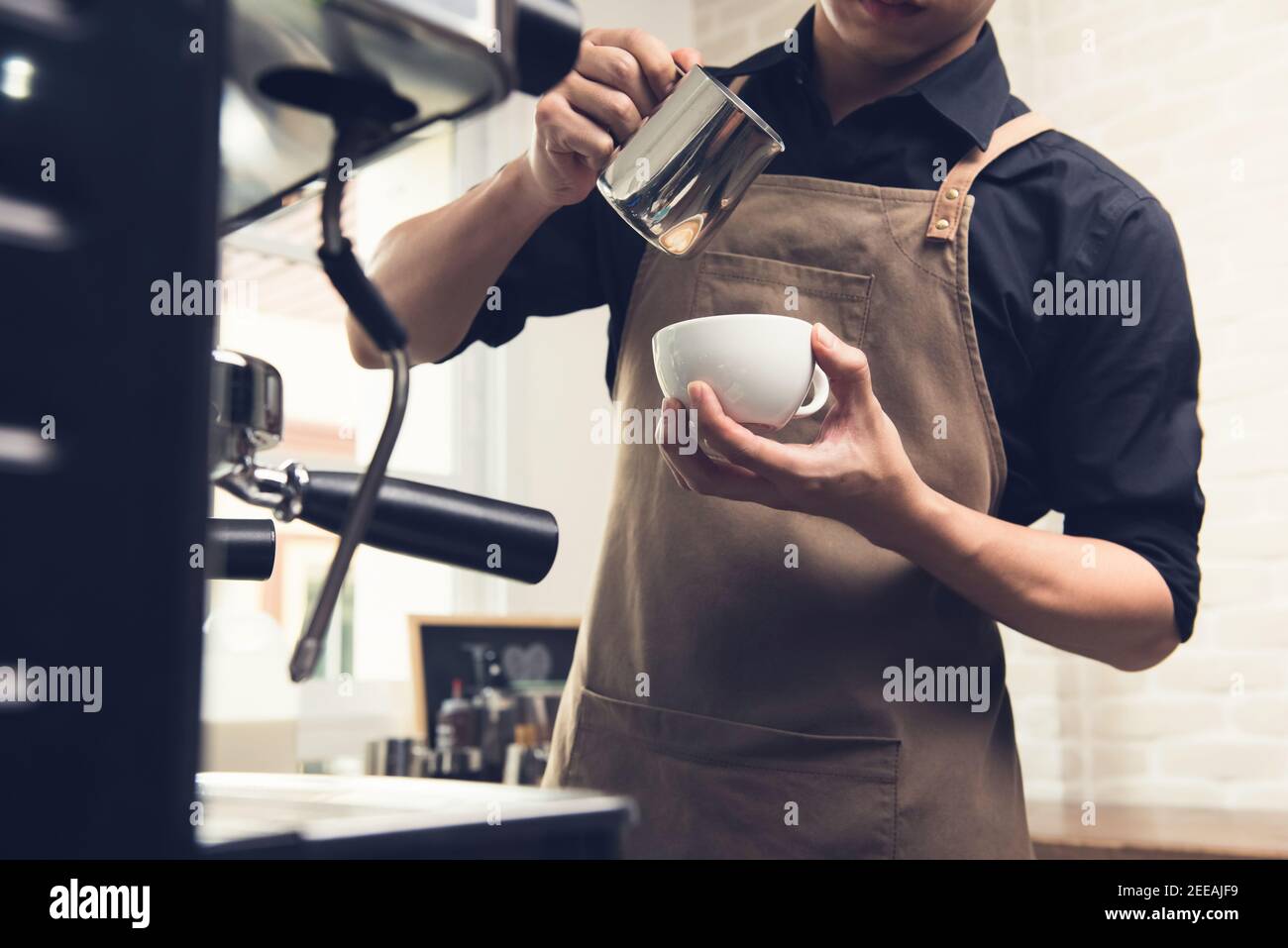 Professioneller Barista gießt gedämpfte Milch in die Kaffeetasse und macht Latte Kunst im Café Stockfoto