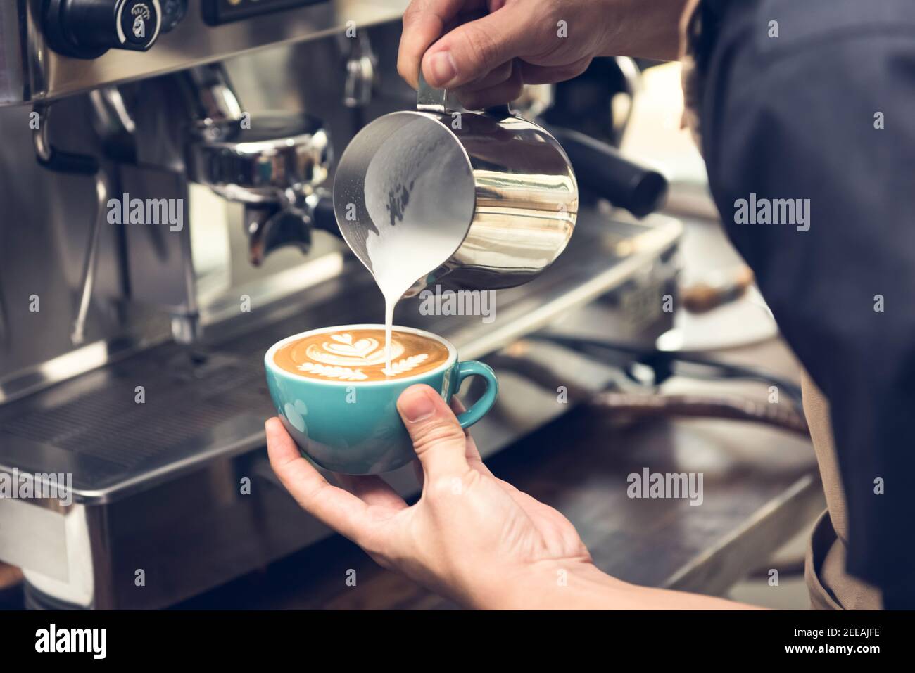 Professioneller Barista gießt gedämpfte Milch in die Kaffeetasse und macht so schön Latte Art Rosetta Muster Stockfoto