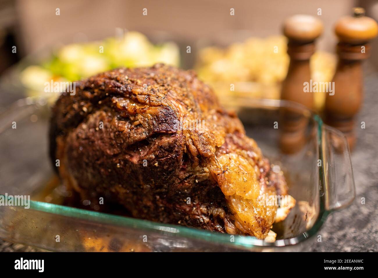 Prime Rib Roastbeef Abendessen mit Salz und Pfeffer Shaker Und Geschirr im Hintergrund Stockfoto