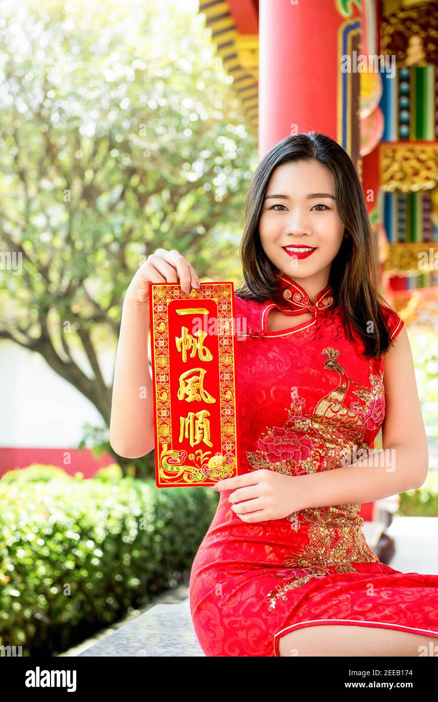 Lächelnde asiatische Frau in traditionellen roten Cheongsam Qipao Kleid zeigt Chinesisches Neujahrsgruß-Textschild sagte alles wird sein Gut Stockfoto
