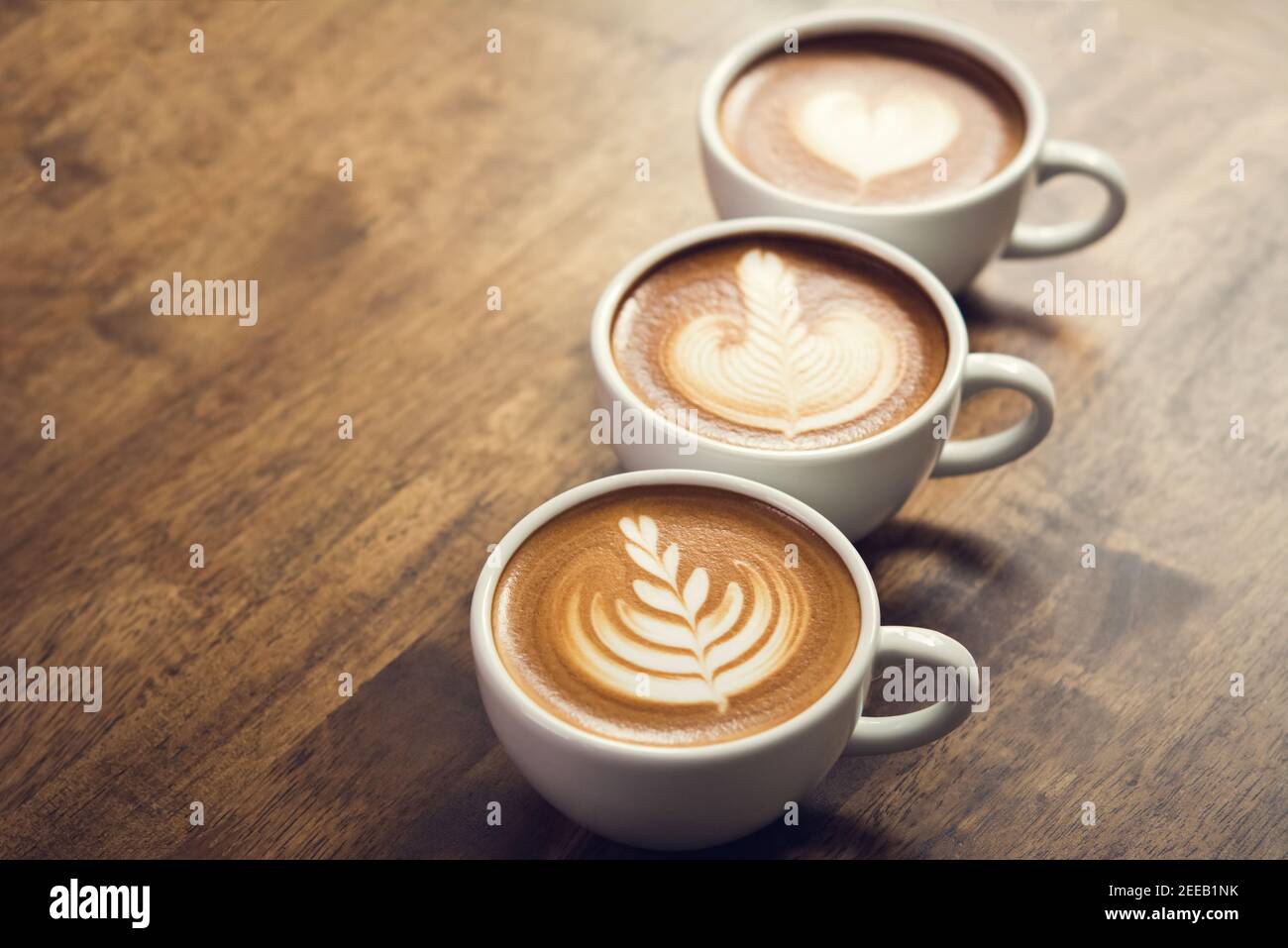 Frisch gebrühte Kaffees mit schöner Latte-Kunst an der Oberfläche, drei Tassen hintereinander auf einem Holztisch zum Trinken bereit Stockfoto