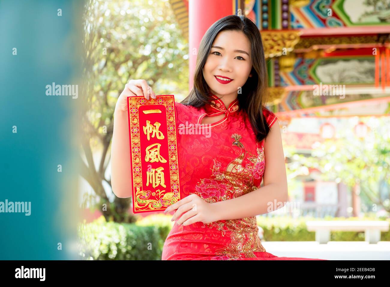 Lächelnde asiatische Frau in traditionellen roten Cheongsam Qipao Kleid zeigt Chinesisches Neujahrsgruß-Textschild sagte: "Alles wird sein Gut“ Stockfoto