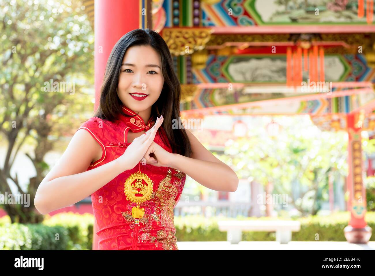 Lächelnde asiatische Frau in traditionellen roten Cheongsam Qipao Kleid machen Gruß mit chinesischen Neujahrsgruß Schild in der Hand sagte 'Glück und gute Fortun Stockfoto