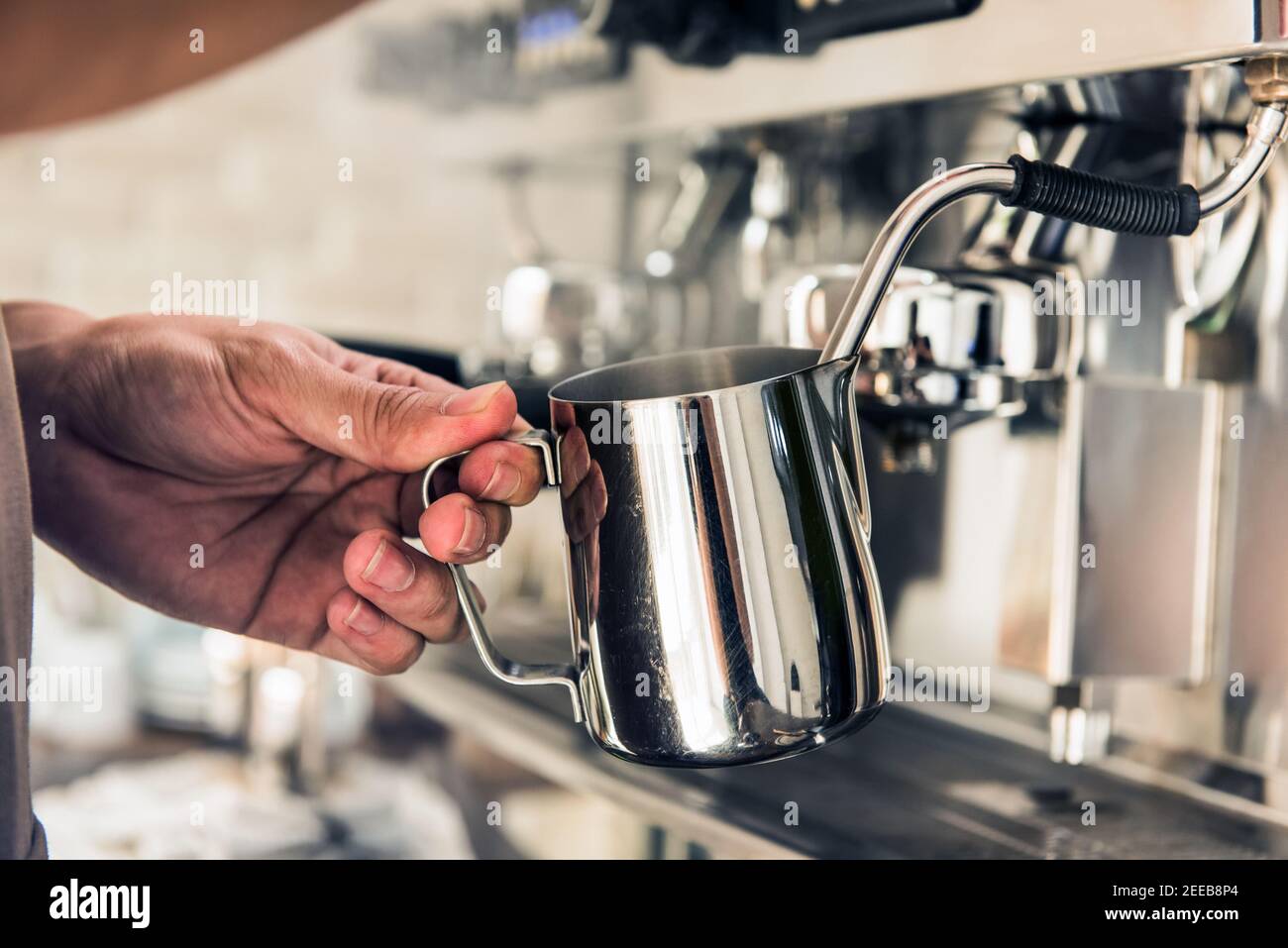 Barista dämpft Milch im Krug mit Kaffeemaschine Um Latte Kunst im Café zu machen Stockfoto