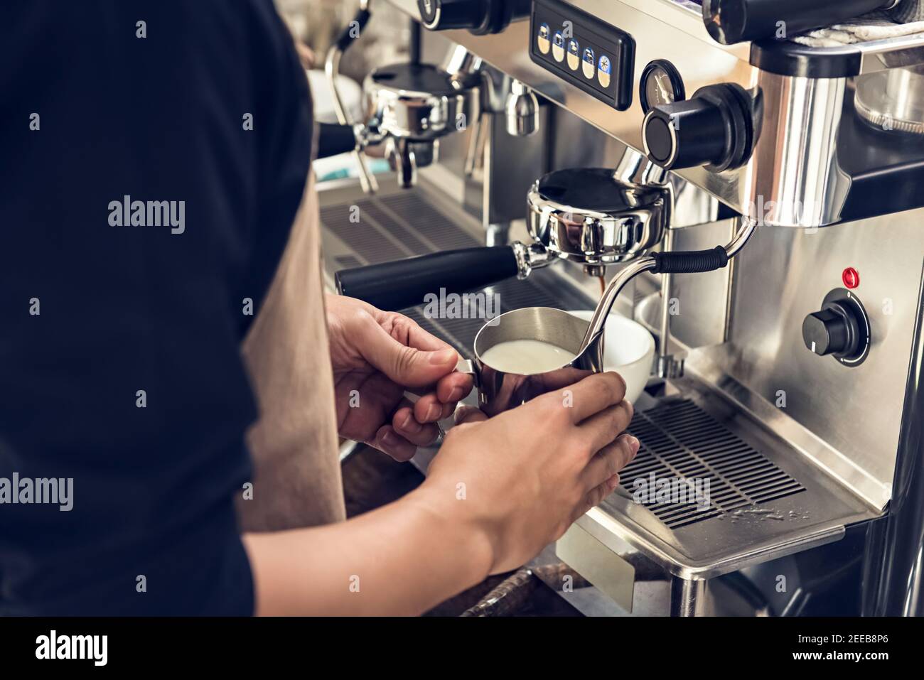 Barista dämpft Milch im Krug mit Kaffeemaschine Um Latte Kunst im Café zu machen Stockfoto