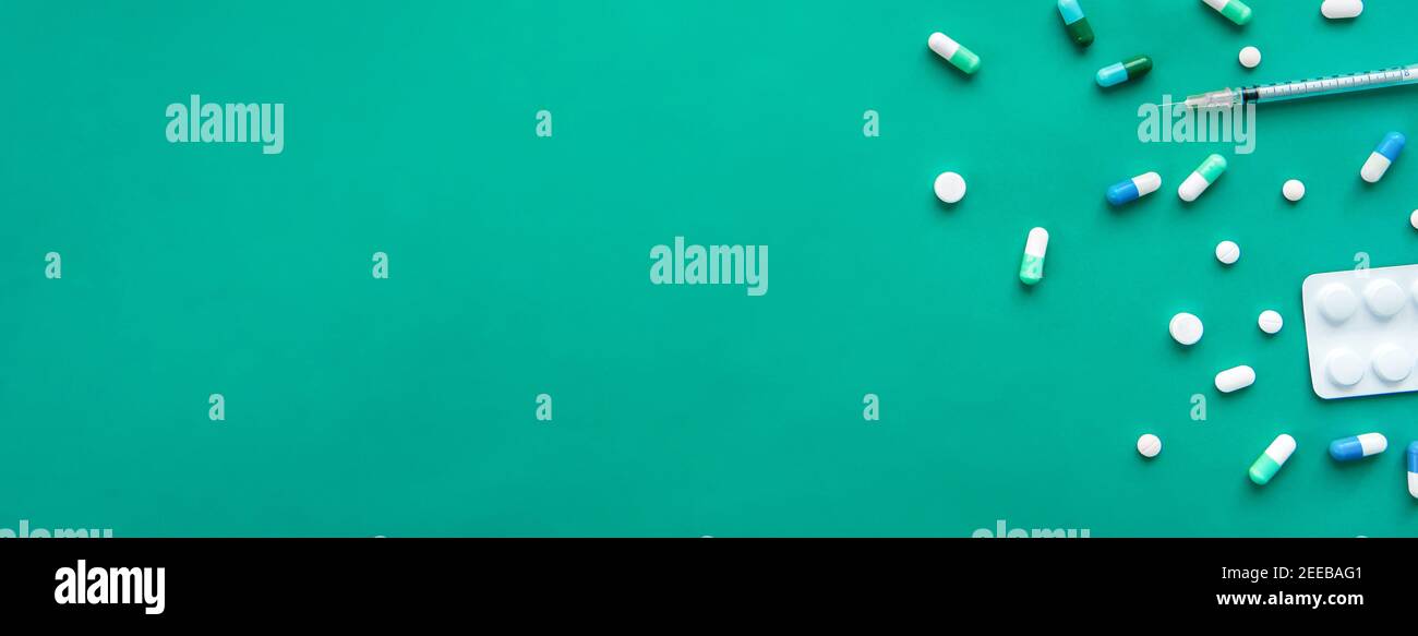 Medikamente und Spritze am Rand von Grünpapier, medizinisches Hintergrundkonzept, Panorama-Banner mit Kopierraum Stockfoto