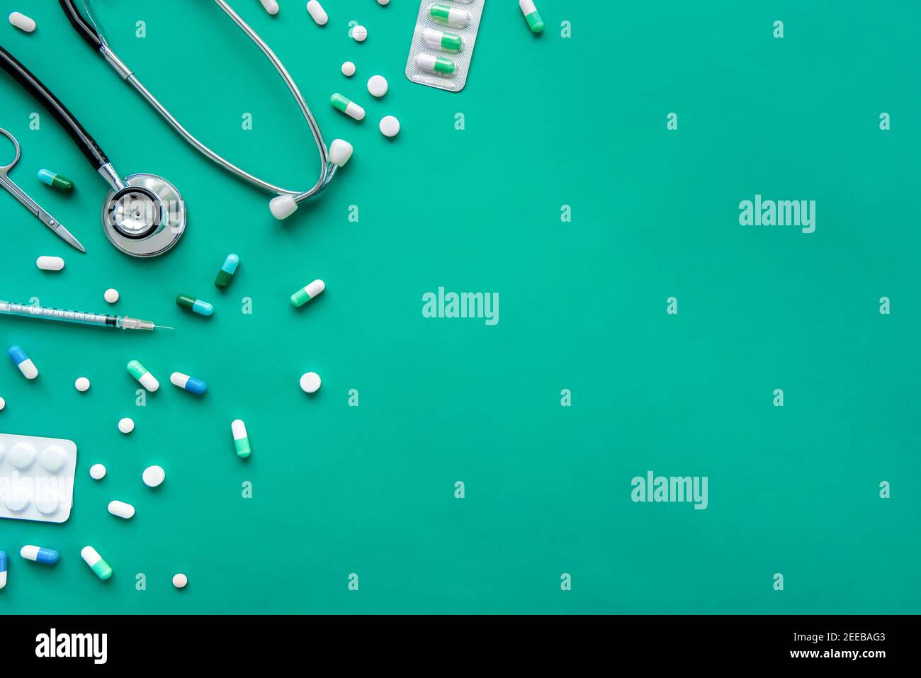 Pillen und medizinische Nachbauten einschließlich Stethoskop, Spritze und Schere am Rand auf grünem Hintergrund, Draufsicht mit Kopierraum Stockfoto