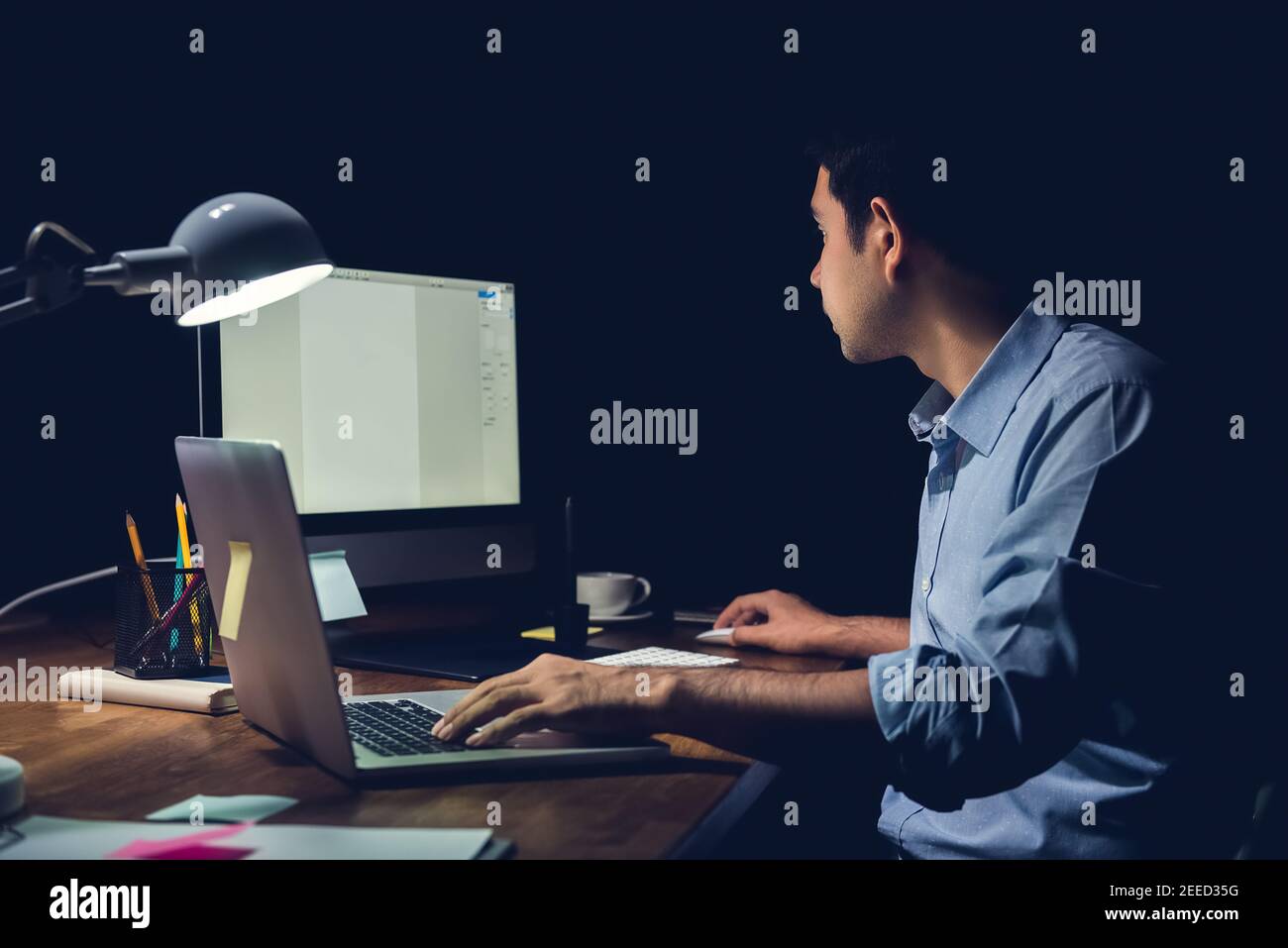 Junger Geschäftsmann, der spät in der Nacht im Büro Überstunden hat Der Schwerpunkt liegt auf der Arbeit mit dem Computer an seinem Schreibtisch Stockfoto