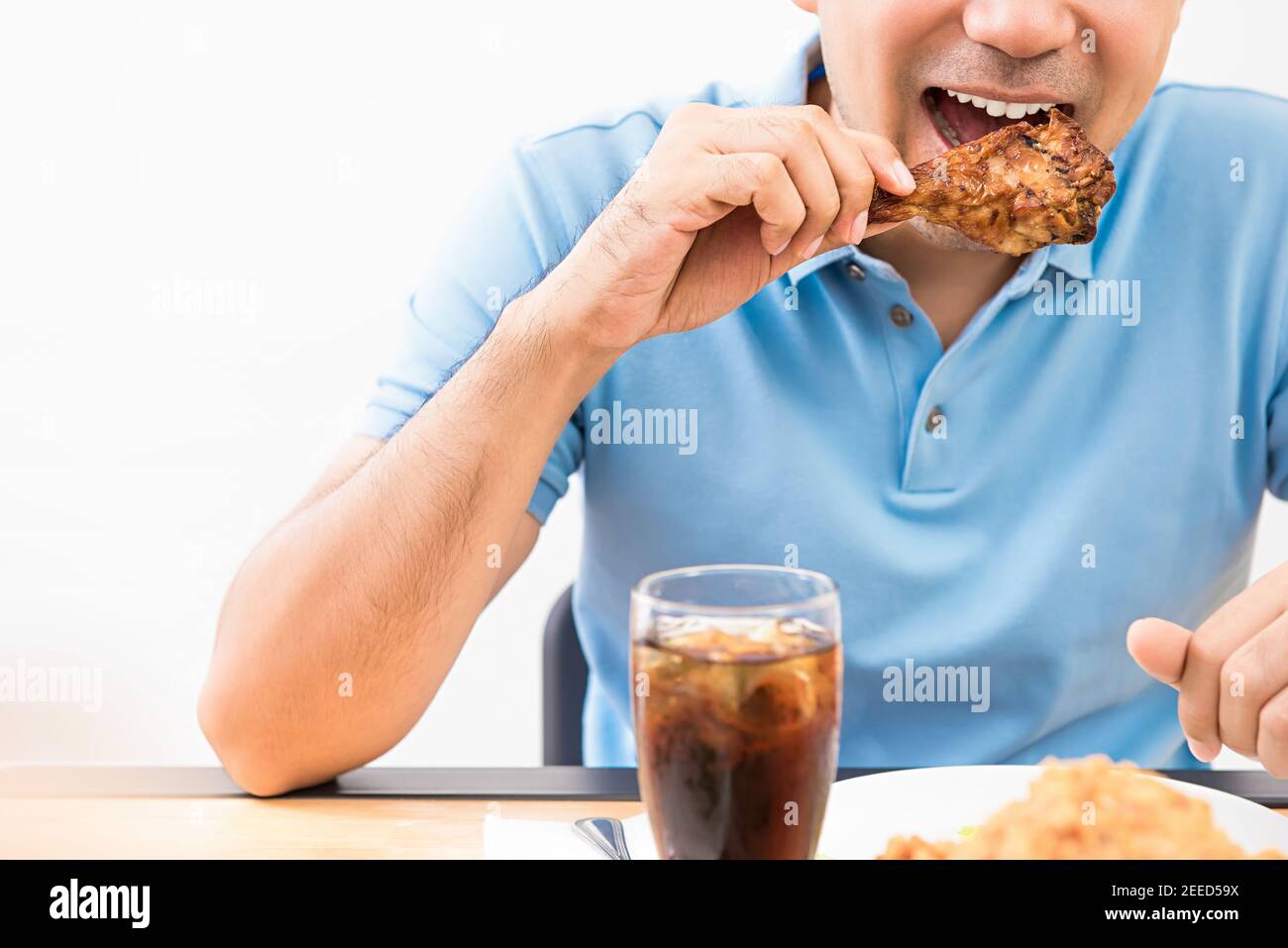 Ein junger Mann isst gerne gegrillten Hähnchendrumstick mit einem alkoholfreien Getränk in einem Restaurant. Stockfoto