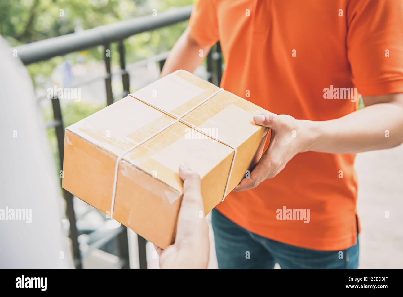 Ein Liefermann in orangefarbener Uniform überreicht einen Paketkasten An einen Kunden - Kurierservice-Konzept Stockfoto