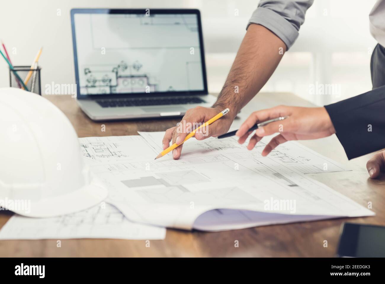 Architekten- oder Ingenieurteam, das ein Projektdesign anhand von Bauplänen und einem Laptop-Computer im Büro diskutiert, bevor es die Baustelle besucht. Stockfoto