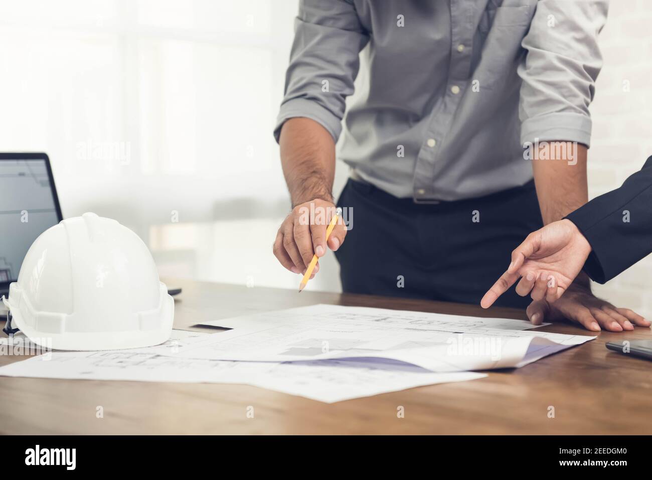 Architekten- oder Ingenieurteam, das ein Projektdesign anhand von Bauplänen und einem Laptop-Computer im Büro diskutiert, bevor es die Baustelle besucht. Stockfoto