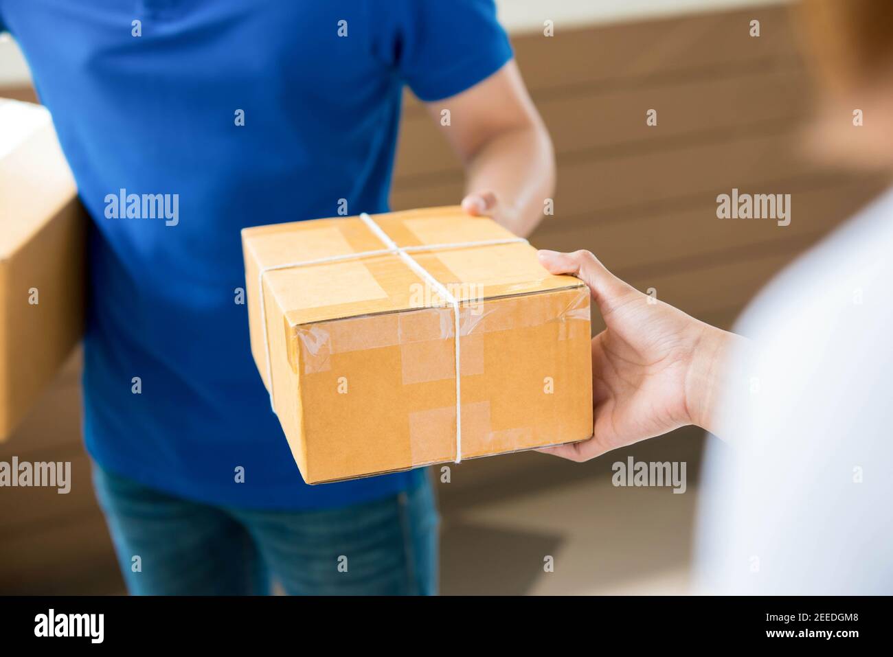 Ein Mann in einem blauen Hemd liefert eine Tür zu Tür Lieferung Paket an eine Frau Stockfoto