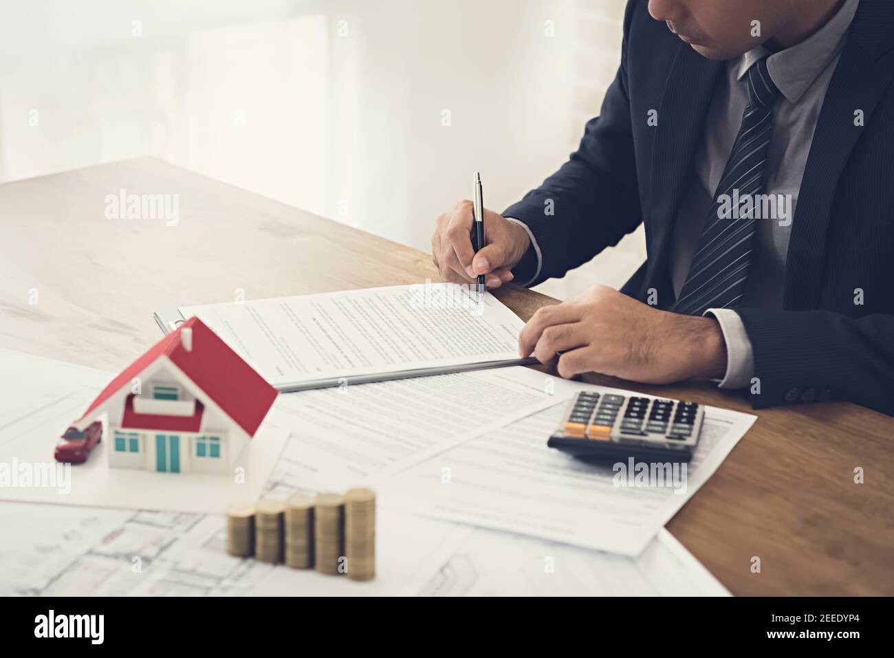 Geschäftsmann Unterzeichnung Vertrag mit Dokument, Geld und Hausmodell auf dem Tisch - Immobilien, Immobilien und Anlagekonzepte Stockfoto