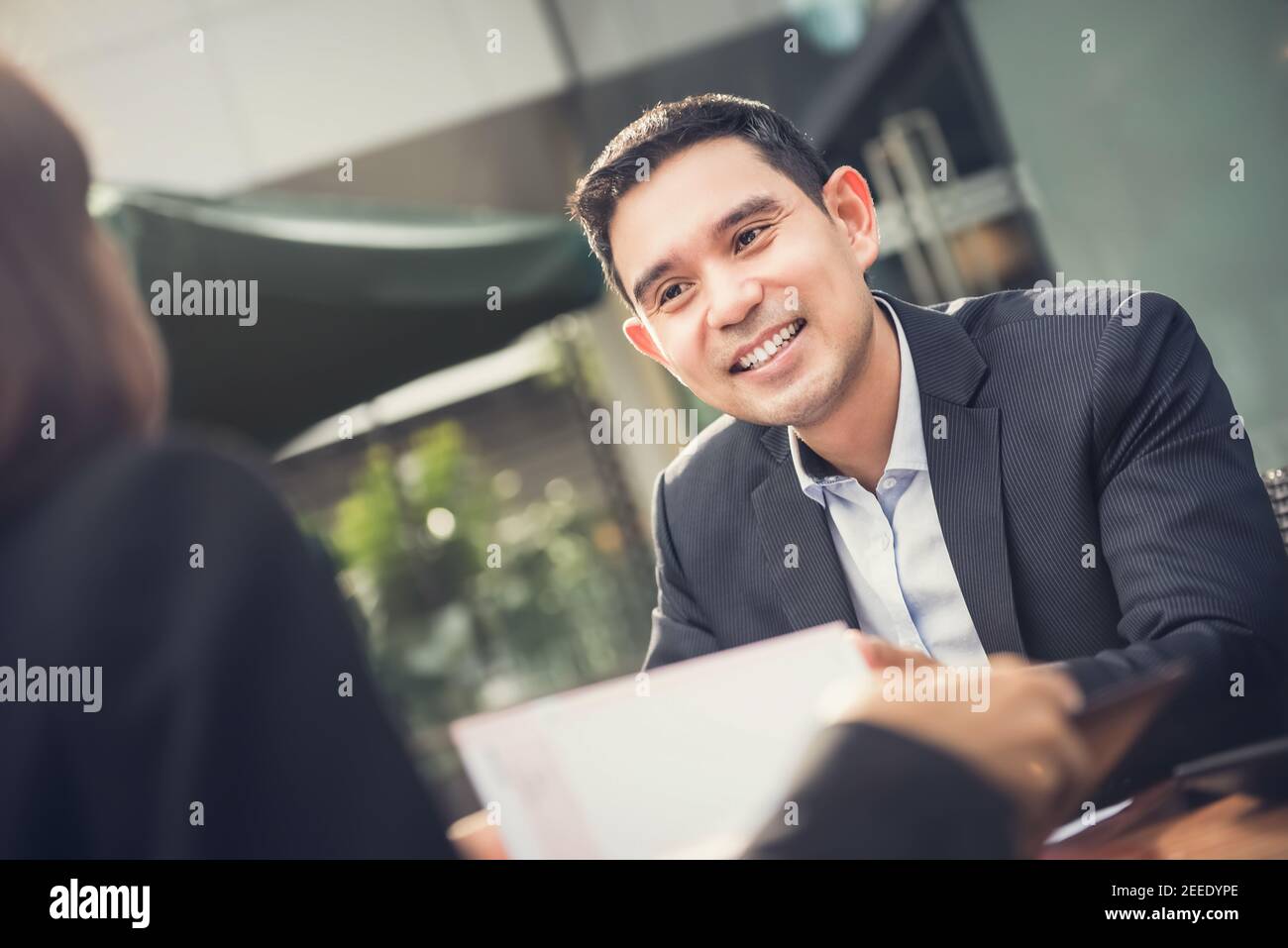 Fröhlich lächelnder asiatischer Geschäftsmann, der sich mit dem Kunden im Café trifft Stockfoto