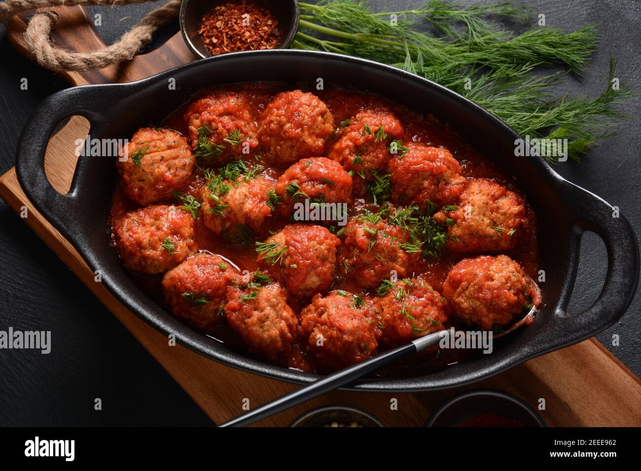 Boulettes de Poisson, gebratene Fischbälle in Tomatensauce in einer schwarzen Schale auf einem Betontisch mit Zutaten Stockfoto